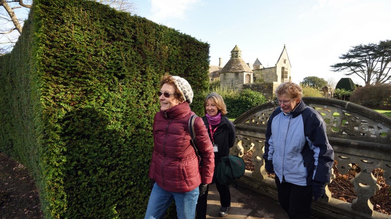 Three people in winter clothes walking by a hedge with part of the property behind them